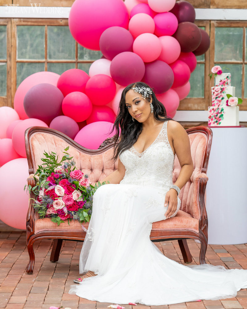 Bride sitting on a sofa surrounded by pink balloons